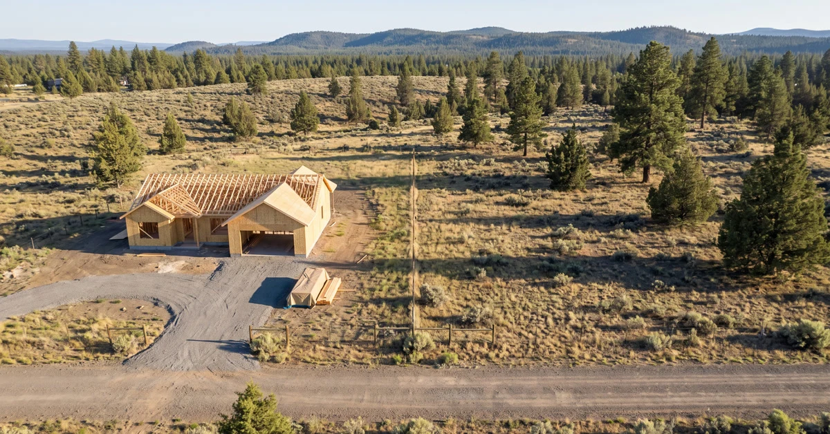 Aerial view of two adjoining rural lots in Central Oregon pine and juniper country, a house being framed on one and open ground on the other.